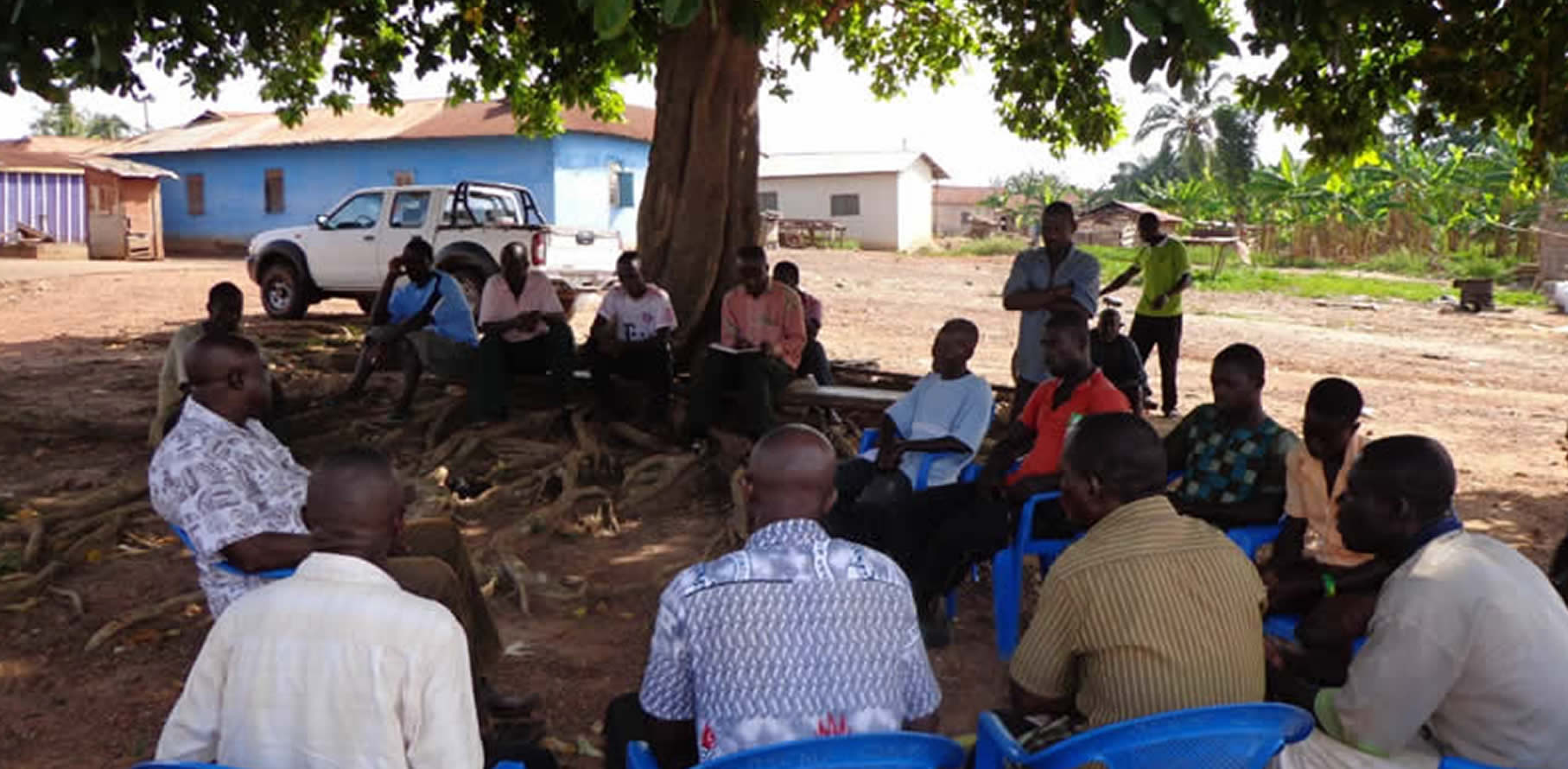 Men gathered outdoors under a tree for a community meeting in Ghana